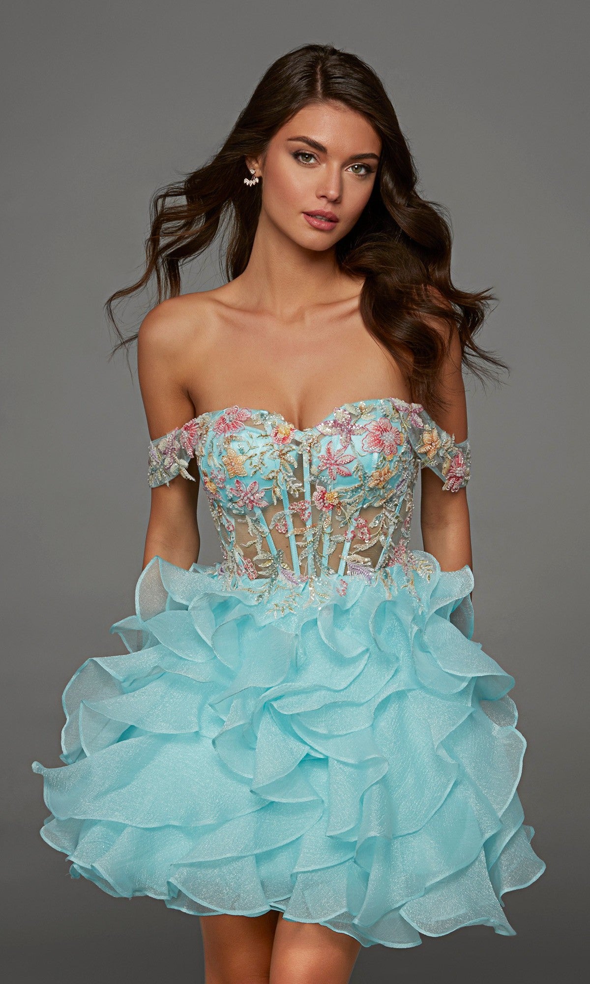 A woman wearing the Alyce 30087 short homecoming dress in Sea Glass, a strapless fit-and-flare design featuring ruffled layers and a sheer bodice with delicate beaded floral embroidery, stands against a plain gray background.